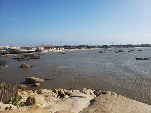 Vista da Praia da Pedra do Sal em Parnaíba, PI, com suas rochas características, barcos de pesca ancorados no mar e a vila de pescadores ao fundo.