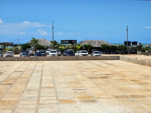 Vista a partir de estacionamento no complexo Al Mare, Luis Correia, mostrando estacionamento com veículos e o Beach Bar na praia ao fundo, em dia de sol.
